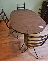 Photo showing oval wood grain dining table with four ladder-back swivel chairs with goldenrod cushions around it.