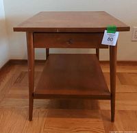 Front view of Paul McCobb side table showing rectangular top, tapered legs, lower shelf, and single drawer with brass conical pull.