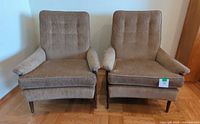 Front view of two brown upholstered mid-century modern chairs with wood legs, placed side by side.
