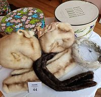 Two mink hats, two mink collars, mink headband with veil, and two vintage hat boxes arranged on white surface