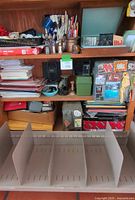 Wooden shelving unit with various office supplies, stacks of papers, folders, and vintage magnet collection. Large beige metal desk organizer shelf shown in front of the unit with compartments.