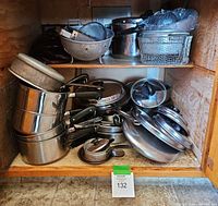 Shelf filled with stacked pots and pans, including metal strainers and lids.