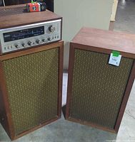 Two mid-century modern wooden cabinet speakers side by side with green patterned fabric grilles