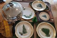 Photo showing three Lenox Christmas plates (1976, 1977, 1978) with evergreen tree designs, a silver-plated covered dish with engraved lid, and packaging ribbons