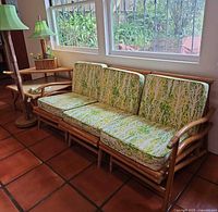 Overall view of three-seat bamboo couch with cushions, floor lamp and table lamp on side table