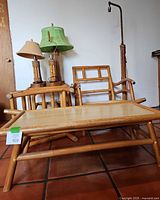 Photo showing four bamboo table lamps with different lampshades, bamboo chair, side table and bamboo standing floor lamp in background. Bamboo coffee table in foreground.