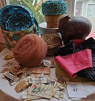 Overall lot featuring pink rose net hat, blue braided raffia hat, two vintage hat forms, millinery fabric scraps, and numerous vintage hat labels spread across table with floral hat boxes behind.