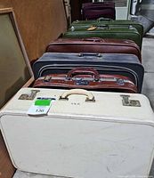 Seven vintage suitcases in a row showing various exterior colors and styles in a storage space.