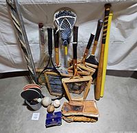 Photo showing the full lot of vintage sports equipment including bats, rackets, gloves, balls, lacrosse stick, and ping pong paddles.