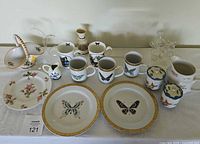 Full view of dishes, mugs, pitchers, jars, and glass swans on display showing complete lot contents.