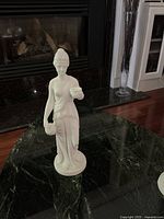 Photo of the female statuette on a black marble surface near a fireplace.