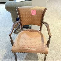 Full front view of an armchair showing solid wood frame and upholstered seat with visible tear.