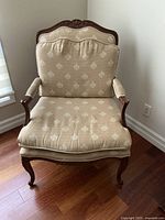 Front view of beige patterned upholstered armchair with dark carved wooden frame and cushion on seat and backrest.