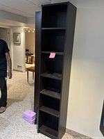 Dark wood bookshelf with five shelves placed upright in a carpeted room with a person partially visible to the left.