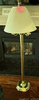 Full view of brass floor lamp showing pleated cream lampshade, brass stem, and decorative hexagonal base.