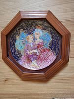 Photo of one collector plate featuring a woman in blue and pink holding a child, mounted in an octagonal wooden frame