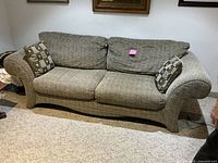 Front view of gray fabric 3-seater couch with rolled arms and patterned throw pillows on a carpeted floor.