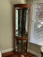 Full view of the curio cabinet positioned in a corner with details of glass shelves and mirrored back panels visible through the glass.