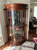 Front view of wood curio cabinet with glass front and sides, showing interior glass shelves.