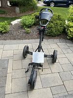 Front view of ClicGear folding golf push cart with three wheels on patio tiles, showing handle and front wheel.