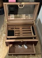 Top view of the humidor cigar box with lid open, showing wood interior compartments for cigars and accessories, and the bottom drawer open with key and plastic accessories inside.