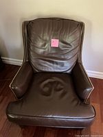 Front view of brown leather armchair showing padded seat, backrest, armrests, and gold stud detailing