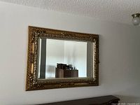 Front view of the large rectangular mirror with ornate gold frame mounted on the wall, showing its detailed carving and size relative to furniture.