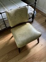 Front-angle view of the retro chair showing the cushioned wide seat and slightly curved backrest with button tufting, wooden legs visible.