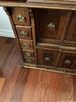 Close-up showing detailed woodwork, small drawers with ornate brass handles on left side, and paneling on cabinet doors.