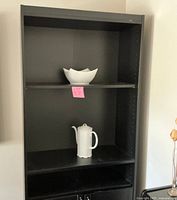 Front view of the shelving unit with upper shelves and lower cabinet, showing white ceramic decorative items on shelves (not included).