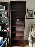 Full view of the dark reddish-brown 5-shelf wooden shelving unit next to a couch and another shelving unit.