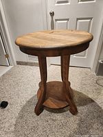 Full view of solid wood round side table showing curved legs and lower shelf