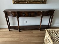 Front view of wood console table showing four drawers, polished dark brown finish, curved edges, and decorative carved legs.