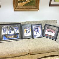 Four framed sports memorabilia items on beige couch: signed James Van Riemsdyk stick blade and photos, Bryan McCabe photo, Bobby Orr photo, 2004 World Cup Champions framed team photo