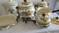 Group shot of enamel cookware showing lattice casserole, stacked warmer set, oval dish, saucepan and daisy casserole