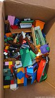 Top-down view of cardboard box filled with mixed Lego pieces in various colours and shapes
