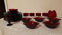 Full view of ruby red glass set showing stacked plates, bowls, stemware and decorative vessel