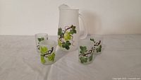 Pitcher centered with four matching glasses showing hand-painted leaf design