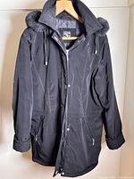 Front view of black 3/4 length winter coat with zipper and snap button closure, fur trimmed detachable hood, left side zippered pocket, and cuff straps.