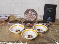 Photo showing three ceramic dessert plates with images of desserts (including tiramisu and cannoli) and three ceramic bowls with orange/yellow striped rim and vegetable images.