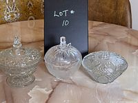 Front view of three lidded candy dishes: cut crystal with pointed knob, clear glass with vertical cuts and square knob, pressed glass with starburst pattern and round knob.