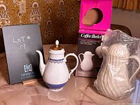 Photo showing white porcelain coffee pot with blue and gold decoration next to Coffee Butler coffee carafe in original box and wrapped in plastic.