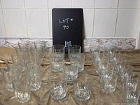 Full lot with all 31 glasses arranged in rows by size and type on a cloth surface, tile backsplash in background.