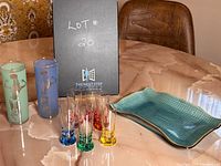 Photo showing two highball glasses, six colored liqueur glasses and green serving plate on table.