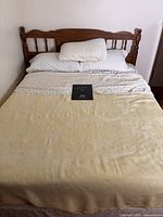 Front view of wooden double bed with headboard and rails, covered with bedding for reference only