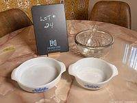 Photo of two white milk glass casserole dishes with blue floral details on the sides alongside a clear glass bowl with silver plate rim and glass pestle, displayed on a round table.