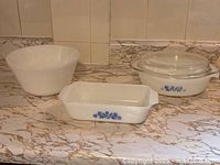 View showing white mixing bowl, two oval casserole dishes with lids, and loaf pan with blue floral decoration.