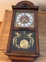 Front view of a vintage 31-day carillon mantle clock showing wooden case, Roman numeral clock face, and pendulum design with gold swans.