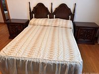 Double bed headboard, rails with mattress and two wooden night stands on either side, bedspread on mattress.