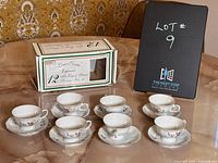 Seven porcelain espresso cups each paired with a matching saucer arranged on a table, with original box nearby.